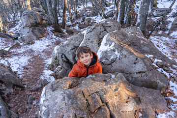 Boy 8 years old white caucasian smiling looking out from behind a large stone in the mountains in winter