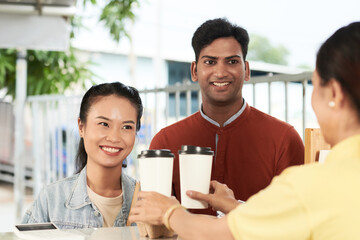 Happy diverse young couple ordering take out coffee in coffeeshop