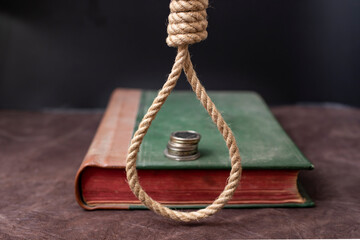 hangman noose over an old book cover with a stack of coins, on a dark background 