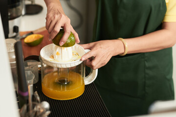 Hands of coffeeshop worker making fresh orange juice for customer