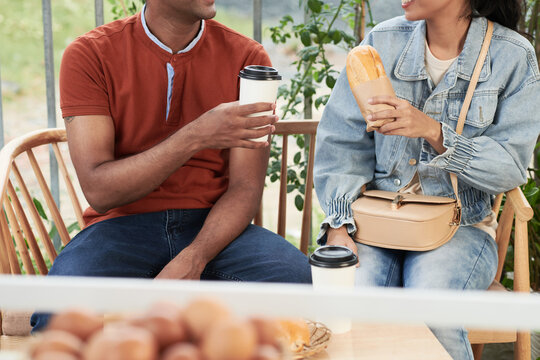 Cropped image of young couple drinking coffee and eating sandwiches at outdoor cafe table