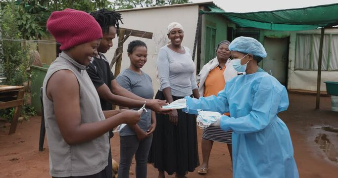 Black African female nurse hands out protective face masks to people in a rural settlement to prevent Covid-19