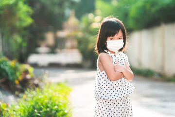Girl wearing white medical face mask stands with her arms crossed. Child are upset. Empty space to enter text.