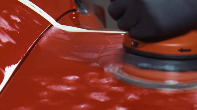 Detailing a red sports car with a red polishing machine. Close up.