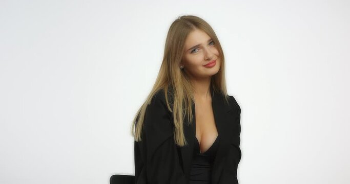 Beautiful woman in a black shirt with long blond hair looks at her manicure and nods her head. Caucasian female model in the studio on a white background. Beautiful female face.