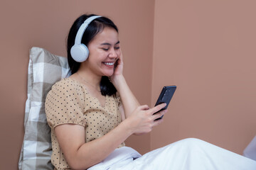 Young woman smiling cheerfully while wearing headphones and holding cell phone in room