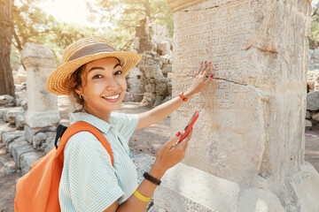 Obraz premium Girl traveler walks through the ancient ruins of the antic Greek city of Phaselis in Turkey. Using virtual audio guide in her smartphone app