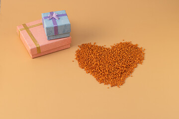 Heart shape with boxes of gifts on an orange background. The figurine is made of bright orange shiny beads. Valentine's day signs and symbols for copy space. Festive mockup.	