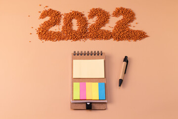The number 2022 next to a notebook and a planning pen. The figure is made of bright orange shiny beads. Signs and symbols of the new year for copy space. Festive mockup.