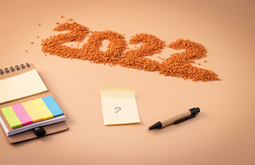 Number 2022, notepad, pen and sheet of paper with a question mark. The figurine is made of bright orange shiny beads. Signs and symbols of the new year for copy space. Festive mockup.