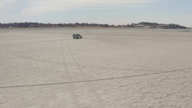 4x4 Car Driving On Dry Salt Pan Of Makgadikgadi Towards Kubu Island (Ga'nnyo) In Botswana, South Africa. - aerial follow