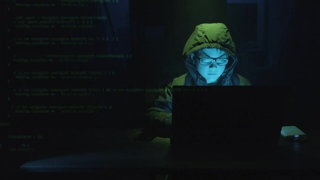 Computer Code Superimposed Over Male Kid Hacker At Work On A Laptop Software At Night. medium shot, zoom-in