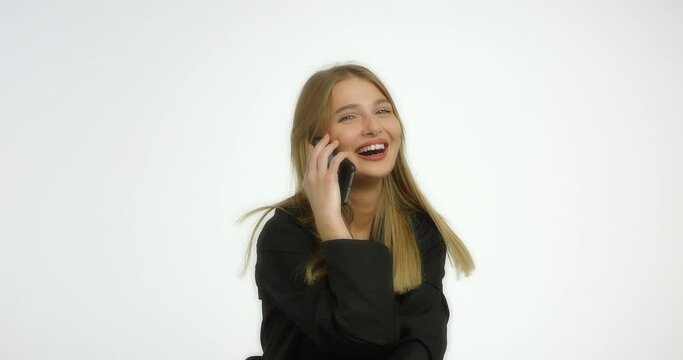 Happy woman with long blond hair is talking on the phone and laughing. Girl model straightens her hair and smiles in the studio at the camera in the studio on a white background.