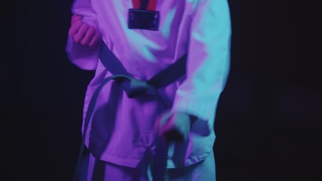 A little boy doing taekwondo in neon lighting - showing moves with his hands