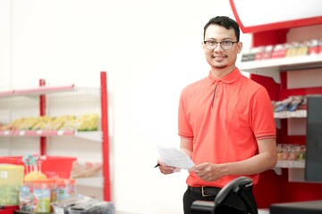 Smiling  supervisor making notes to the clipboard while standing near a rack of mixed goods.