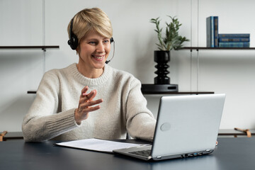 Smiling middle-aged modern woman wears a headset, a distance course, or training on a laptop.