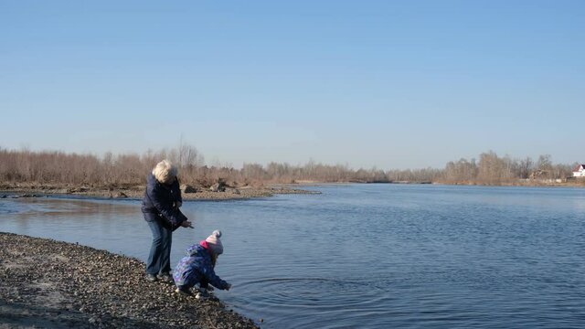 Grandmother and grandchild  throws  stones into the river. Activity  outdoors