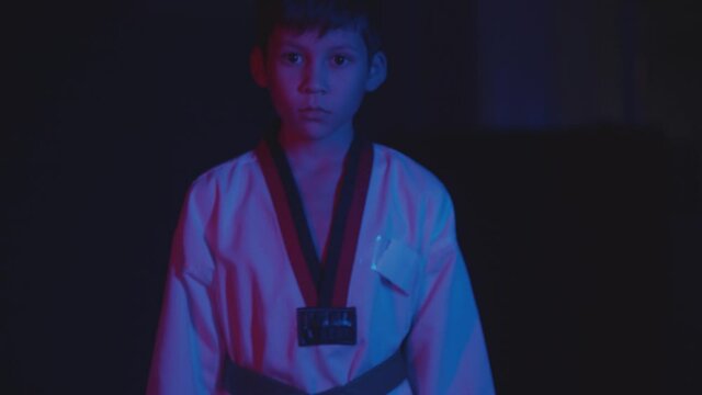 A little boy doing taekwondo moves in the dark with neon lighting