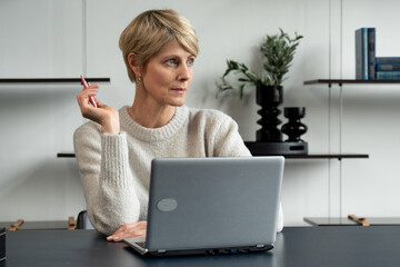 A focused middle-aged woman entrepreneur thought deeply while working at a desk in a modern office...