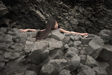 Art portrait of asian girl relaxing on black basalt lava rocks in Vik, Iceland