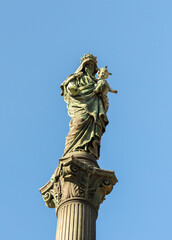 The upper part of the statue of the Virgin Mary with a baby in her arms stands on a high pedestal...