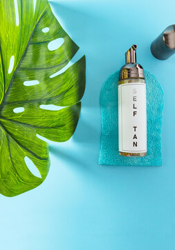 Gradual self tan lotion and  tanning mitt on blue background with monstera leaf.Tan Without Sun concept