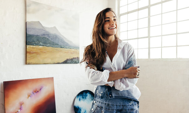 Happy female artist standing in front of her paintings