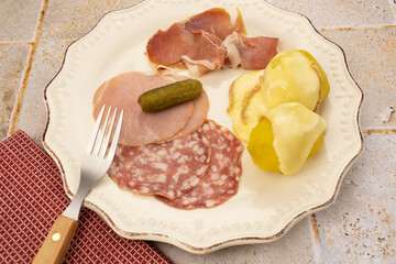 fromage à raclette fondu sur des pommes de terre et charcuterie dans une assiette