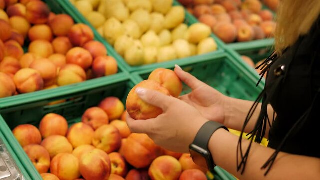 Close-up of a young woman buying fresh fruit at a grocery store, she is holding a nectarine in her hands.