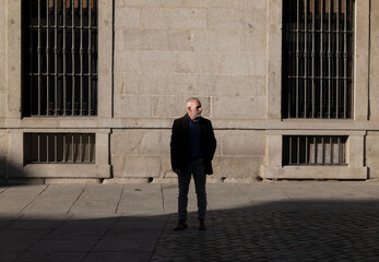Adult man in suit standing on street against wall with sunlight and shadow