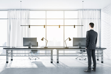 Pensive european businessman standing in modern concrete office interior with window and city view, furniture, equipment and daylight. Workplace, CEO and executive concept.