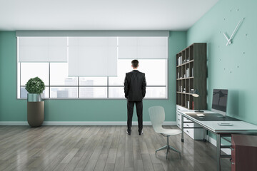 Thoughtful european man standing in modern blue office interior with wooden flooring, furniture, equipment and daylight. Workplace, CEO and executive concept.