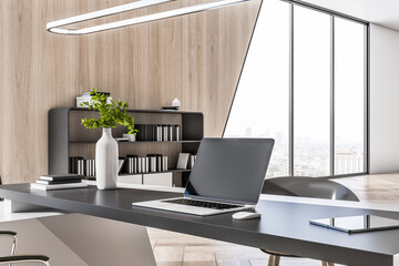 Close up of empty laptop screen on desktop in modern wooden and concrete designer office interior with furniture, window with panoramic city view. 3D Rendering.