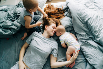 Mommy with two small children lies on the bed in the morning and enjoys relationships and motherhood