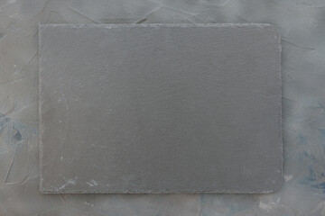 Slate plate on dark gray stone texture background. Kitchen stone tray for serving food. Black granite rectangle board. Empty space for menu or recipe. Top view copy space, mockup