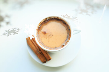 A cup of coffee over Christmas bokeh garlands in the house on the table with a sweater in the background and decorations. Winter mood, festive decoration, magical Christmas.