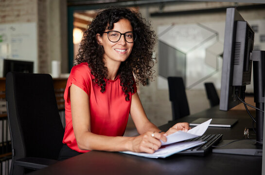 Female professional wearing eyeglasses sitting with documents at desk in office