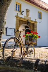 Fototapeta na wymiar A rusty old bicycle with red roses in the back basket and a entrance to an old caslte on a hill in my hometown