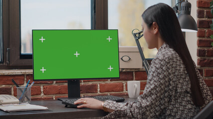 Business woman working with horizontal green screen on monitor at office desk. Entrepreneur using...