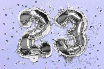 Silver foil balloon number, digit twenty three on a lilac background with sequins. Birthday greeting card with inscription 23. Top view. Numerical digit. Celebration event, template.