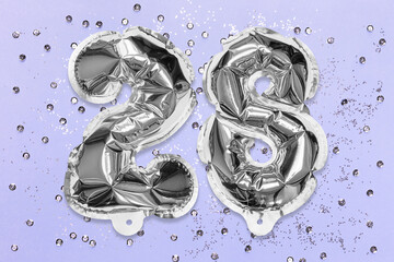 Silver foil balloon number, digit twenty eight on a lilac background with sequins. Birthday greeting card with inscription 28. Top view. Numerical digit. Celebration event, template.