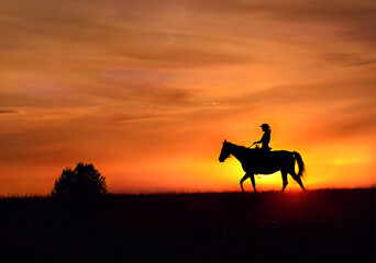 Riding horse at sunset, silhouette. A cowboy girl in a hat rides a horse against the background of a bright red beautiful sunset cloudy sky.