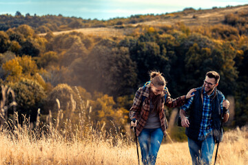 Couple with backpacks hiking together in nature on autumn day.