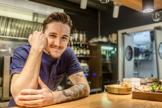 Smiling male bartender standing while leaning on bar counter