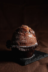 Delicious brown cocoa muffin with sugar powder on slate board on table in studio on dark background 