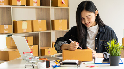 Starting a small business entrepreneur, SME, or freelance Asian woman working with boxes and laptops at home, online sales ideas, e-commerce, shipping, packaging, online marketing, and shipping.