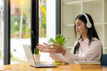 Beautiful Asian student wearing headphones listening to online course development program on...