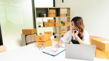 Starting a small business entrepreneur, SME, or freelance Asian woman working with boxes and laptops at home, online sales ideas, e-commerce, shipping, packaging, online marketing, and shipping.
