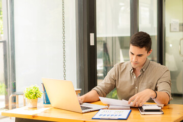 Fototapeta premium young businessman looking at market research report Analyze statistical data in charts. Develop a growth strategy Work on a computer alone in a modern office