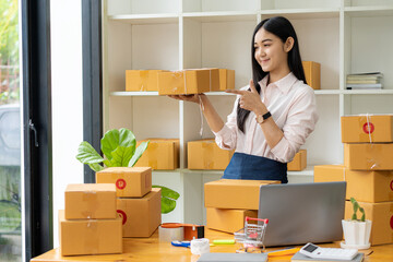 Fototapeta na wymiar Starting a small business entrepreneur, SME, or freelance Asian woman working with boxes and laptops at home, online sales ideas, e-commerce, shipping, packaging, online marketing, and shipping.